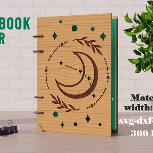 Op de afbeelding: Een houten notitieboekomslag met een lasergesneden ontwerp van een halve maan, sterren en bladeren. De omslag is 3 mm dik en het ontwerp is 300 DPI. De tekst "NOTEBOOK COVER" staat bovenaan de afbeelding.