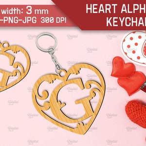 May include: A wooden heart-shaped keychain with a decorative letter G inside. The keychain is made of light brown wood and has a silver metal ring. The background is pink with red hearts and other Valentine's Day decorations.