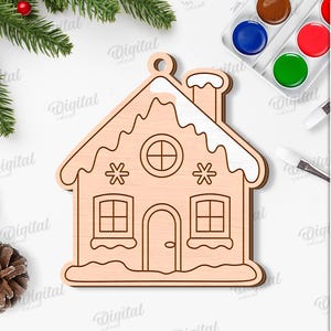 May include: A wooden gingerbread house ornament with a chimney, windows, and door. The ornament is surrounded by Christmas decorations, including pine needles, berries, and a candy cane. The text "SUITED FOR ANY MATERIAL THICKNESS" is visible.