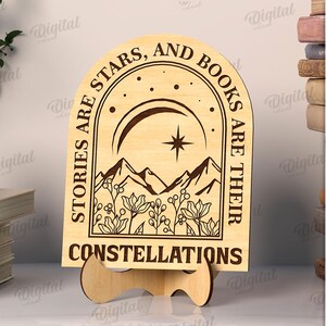 K&ouml;nnte beinhalten: Ein Holzschild mit dem Text "STORIES ARE STARS, AND BOOKS ARE THEIR CONSTELLATIONS" wird auf einem St&auml;nder angezeigt. Das Schild zeigt ein Berg- und Sterndesign. Das Schild ist 3 mm breit. Digitaler Download.