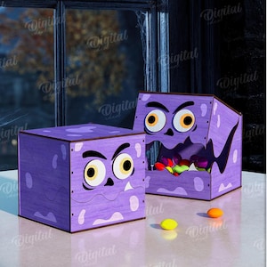 K&ouml;nnte beinhalten: Zwei lila Halloween-Boxen mit Monstergesichtern. Eine Box ist geschlossen, die andere offen und mit bunten S&uuml;&szlig;igkeiten gef&uuml;llt. Die Boxen stehen auf einer wei&szlig;en Oberfl&auml;che, mit einem K&uuml;rbis und einem Fenster im Hintergrund.