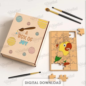 May include: A wooden box and jigsaw puzzle set featuring a parrot design. The box reads "A BOX OF JOY" and has colourful circles. The puzzle is partially assembled. Paintbrushes and a palette are also visible.