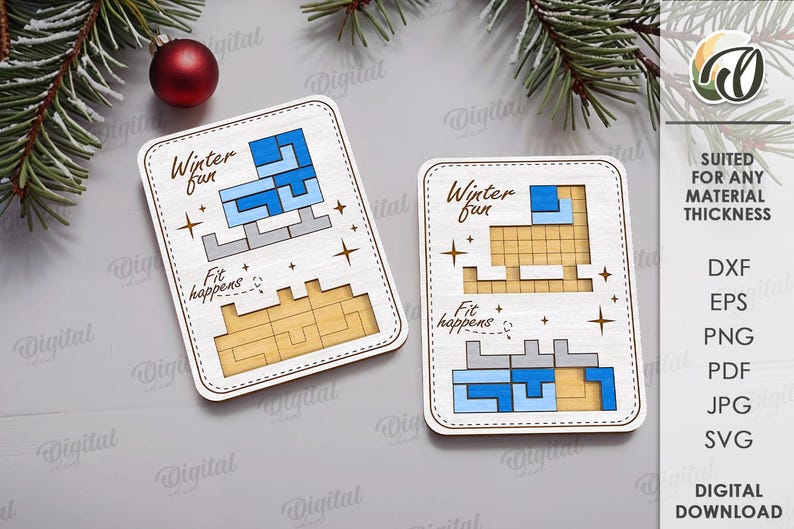 May include: Two wooden puzzles with the text "Winter fun" and "Fit happens". The puzzles feature a blue and gray design, with a light brown base. A red ornament and evergreen branches are in the background.