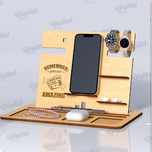 Könnte beinhalten: Ein Handy-Ständer aus Holz mit einem Schlitz für ein Smartphone, Uhrenhaltern und einer Ablage für Zubehör. Auf dem Ständer steht der Text "Remember - you are - AMAZING". Die Materialstärke beträgt 3 mm.