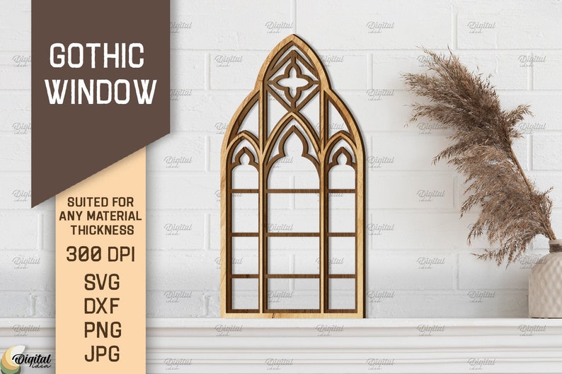 May include: A wooden cutout of a gothic window with a pointed arch and multiple panes. The window is on a white brick wall with a dried grass plant in a white vase.