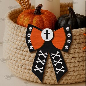 K&ouml;nnte beinhalten: Eine Halloween-Schleife mit Kreuz- und Totenkopf-Design in Orange, Schwarz und Wei&szlig; liegt in einem geflochtenen Korb mit orangefarbenen und schwarzen K&uuml;rbissen. Die Schleife ist mit Totenk&ouml;pfen und gekreuzten Knochen verziert. Der Text rechts lautet "SUITED FOR ANY MATERIAL THICKNESS".