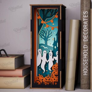 May include: A Halloween-themed shadow box with a spooky scene featuring ghosts, pumpkins, and a haunted house. The box is made of wood and has a black frame with orange accents. The material width is 3 mm.