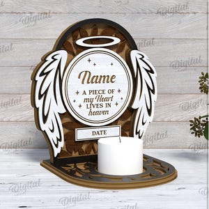 May include: A wooden memorial candle holder with a cutout design of angel wings and a halo. The holder has a space for a name, date, and the text "A piece of my heart lives in heaven".