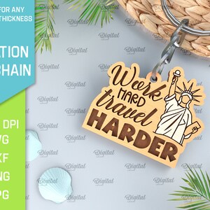 May include: Wooden keychain with a brown background and the text "Work hard travel harder" in a brown font. A white outline of the Statue of Liberty is on the right side of the keychain.