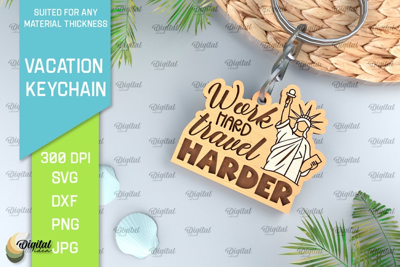 May include: Wooden keychain with a brown background and the text "Work hard travel harder" in a brown font. A white outline of the Statue of Liberty is on the right side of the keychain.