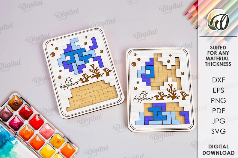 May include: Two wooden puzzle boards with blue and light blue pixelated designs, brown coral accents, and the text "Fit happens." The boards are rectangular with rounded corners. The image also includes a watercolor palette and colored pencils.