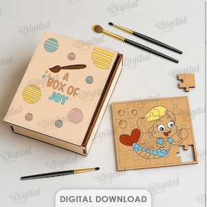 May include: A wooden box with the text "A Box of Joy" and a mermaid puzzle. The box is decorated with colourful circles and a paintbrush icon. Two makeup brushes and a palette are also visible.