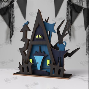 May include: A laser-cut wooden Halloween haunted house decoration. The house is painted in shades of blue and black, with a small blue bird perched on top. The material width is 3 mm.