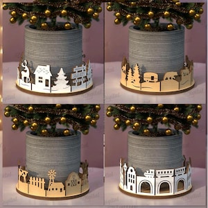 Puede incluir: Se muestran cuatro diseños de macetas para árboles de Navidad, cada uno con una base decorativa diferente. Las bases son de madera y presentan diseños recortados de escenas de pueblo, bosque y granja. El texto de la derecha dice "4 DISEÑOS" y "DESCARGA DIGITAL".