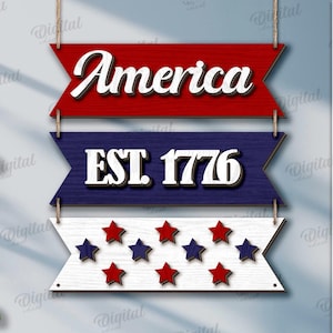 Peut inclure: Panneau en bois patriotique avec trois banni&egrave;res superpos&eacute;es. La banni&egrave;re sup&eacute;rieure indique "America" en blanc sur fond rouge. La banni&egrave;re du milieu indique "EST. 1776" sur fond bleu. La banni&egrave;re inf&eacute;rieure a des &eacute;toiles rouges et bleues.