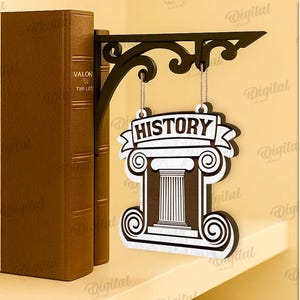 Peut inclure: Un support d'&eacute;tag&egrave;re d&eacute;coratif en m&eacute;tal noir avec une enseigne suspendue qui dit "HISTORY". L'enseigne pr&eacute;sente un dessin de colonne en blanc et marron. Deux livres bruns sont &agrave; gauche.