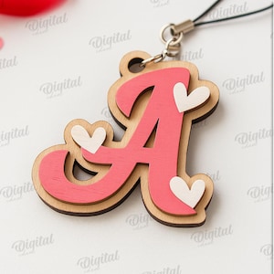 May include: A wooden pendant in the shape of the letter "A", painted pink with a light brown border. The pendant has three small white heart accents. A black cord is attached to the top. The background includes red and pink heart-shaped confetti.