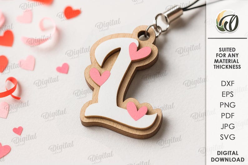 May include: Wooden letter "L" charm with a white overlay and pink heart accents. The charm is attached to a silver-colored lanyard. Scattered around are pink and red heart-shaped confetti. The text "SUITED FOR ANY MATERIAL THICKNESS" is visible.