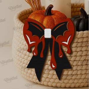 K&ouml;nnte beinhalten: Ein h&ouml;lzerner Halloween-Bogen mit einem Fledermausfl&uuml;gel-Design, schwarzen und roten Akzenten und tropfenden Blutdetails. Der Bogen befindet sich vor einem geflochtenen Korb mit K&uuml;rbissen und anderen Dekorationen. Digitaler Download.