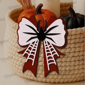 K&ouml;nnte beinhalten: Dekorative Holz-Spinnen-Bogen mit einem schwarzen Spinnen- und Netz-Design. Der Bogen hat ein wei&szlig;es und rotes Farbschema, ideal f&uuml;r Halloween-Dekorationen. Der Bogen ist vor einem geflochtenen Korb mit K&uuml;rbissen platziert.