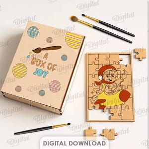 May include: A wooden box with the text "A Box of Joy" and a matching puzzle featuring a cartoon character in a rocket. Paintbrushes and paint surround the box and puzzle. The material width is 3 mm.