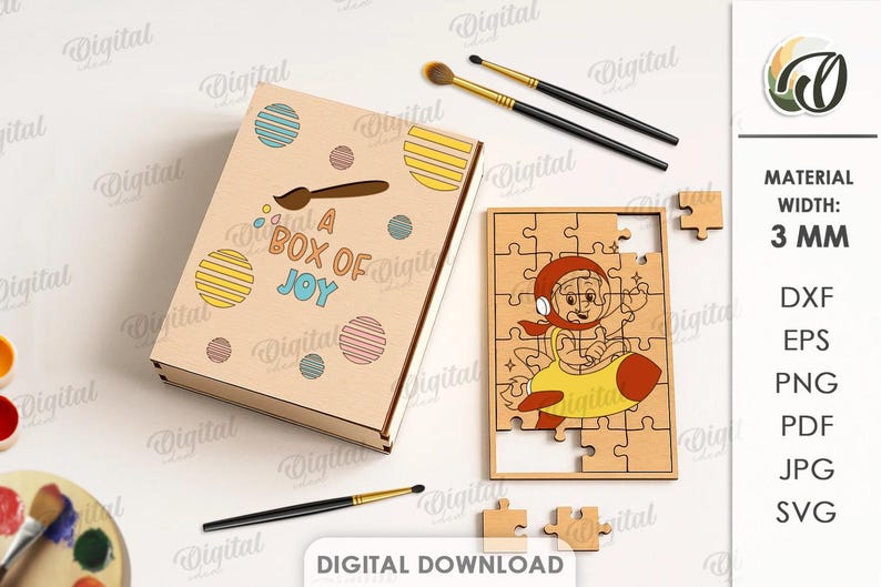 May include: A wooden box with the text "A Box of Joy" and a matching puzzle featuring a cartoon character in a rocket. Paintbrushes and paint surround the box and puzzle. The material width is 3 mm.