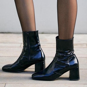 May include: A pair of black patent leather ankle boots with a block heel. The boots have a zip on the inside of the ankle.