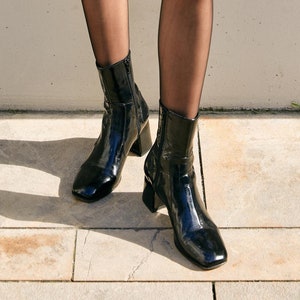 May include: A person wearing black tights and black patent leather ankle boots with block heels.
