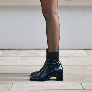 May include: Black ankle boots with a block heel and a pointed toe. The boots are made of patent leather and have a sleek, modern design.