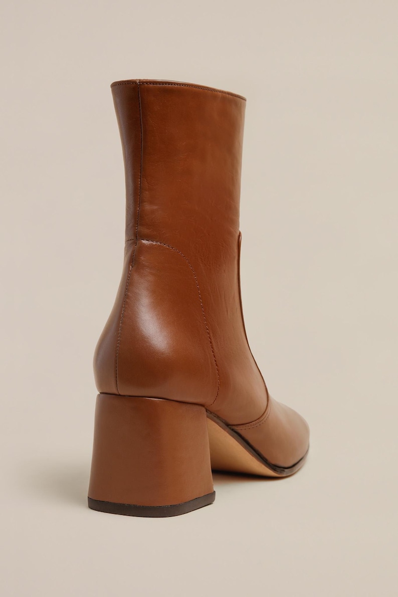K&ouml;nnte beinhalten: Braune Lederstiefel mit Blockabsatz. Die Stiefel haben eine spitze Zehenpartie und einen Rei&szlig;verschluss an der R&uuml;ckseite.