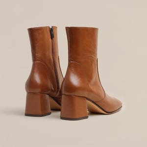 K&ouml;nnte beinhalten: Ein Paar braune Lederstiefeletten mit Blockabsatz. Die Stiefeletten haben eine spitze Zehenpartie und einen Rei&szlig;verschluss an der Innenseite des Kn&ouml;chels.