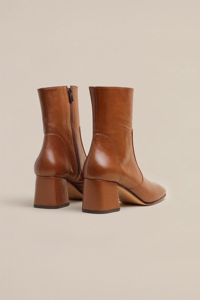 K&ouml;nnte beinhalten: Ein Paar braune Lederstiefeletten mit Blockabsatz. Die Stiefeletten haben eine spitze Zehenpartie und einen Rei&szlig;verschluss an der Innenseite des Kn&ouml;chels.