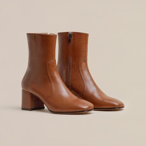 K&ouml;nnte beinhalten: Ein Paar braune Lederstiefeletten mit Blockabsatz. Die Stiefeletten haben einen Rei&szlig;verschluss an der Innenseite jedes Schuhs.