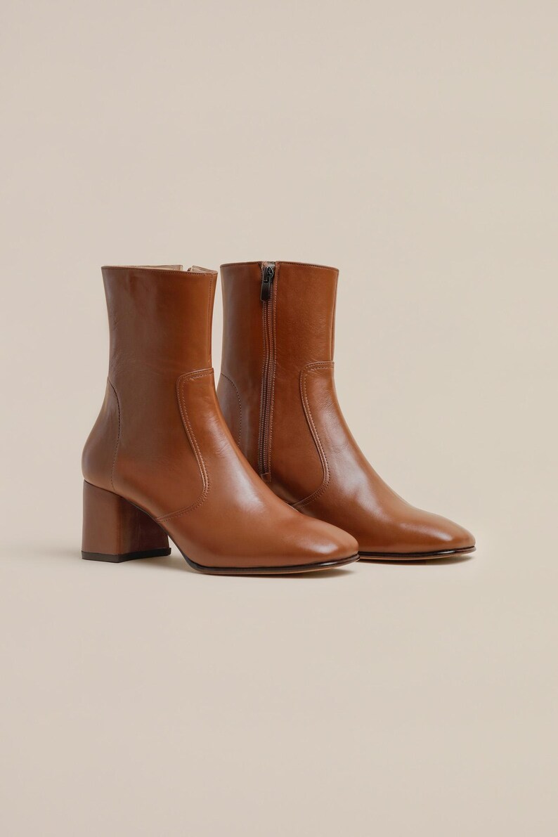 K&ouml;nnte beinhalten: Ein Paar braune Lederstiefeletten mit Blockabsatz. Die Stiefeletten haben einen Rei&szlig;verschluss an der Innenseite jedes Schuhs.