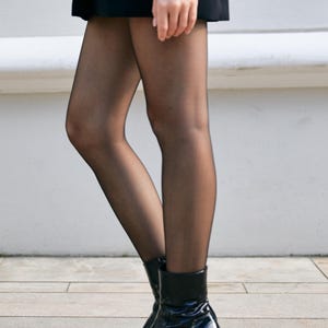 May include: A person wearing black tights and black patent leather ankle boots with a block heel.