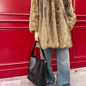 May include: A brown faux fur coat with a button closure, worn with blue jeans and a black leather tote bag.