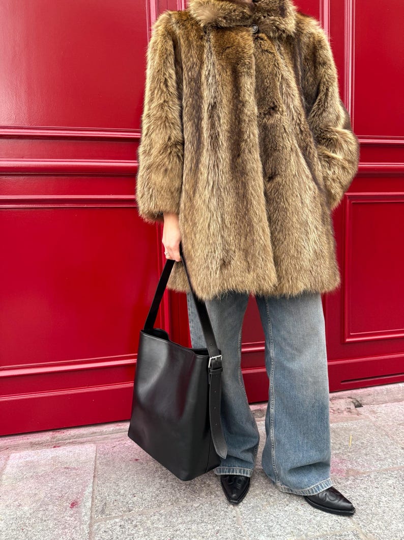 May include: A brown faux fur coat with a button closure, worn with blue jeans and a black leather tote bag.