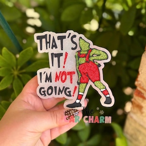 May include: A glittery decorative ornament featuring a green character wearing red pants and black shoes, accompanied by the black and red text that reads: THAT'S IT! I'M NOT GOING! The design has a textured, sparkling finish throughout the entire surface.