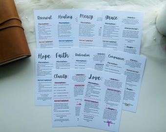 May include: White cards with handwritten titles like "Renewal", "Healing", and "Mercy" are arranged on a white surface. Each card features text and decorative elements in black, blue, and pink. A brown leather journal is visible on the left.