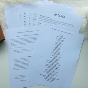 May include: A stack of white printed papers with text, including the word "Patience" and a list of prayer prompts. A brown leather journal and a small potted plant are visible in the background.