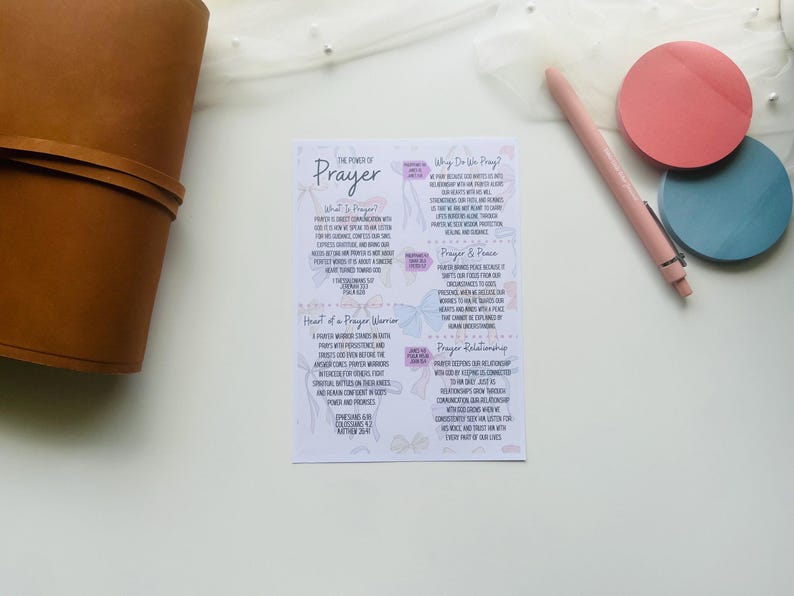 Pu&ograve; includere: Una scheda bianca con il testo "The Power of Prayer" e informazioni dettagliate sulla preghiera. Un diario in pelle marrone, una penna rosa e due sottobicchieri rotondi rosa e blu sono anche nell'immagine.