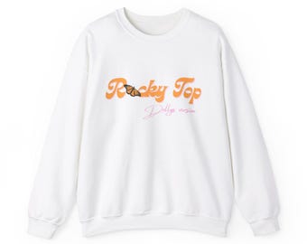 May include: White crew neck sweatshirt with the text "Rocky Top" in orange script, a butterfly graphic, and the text "Dolly's version" in pink script. The sweatshirt is a casual style.