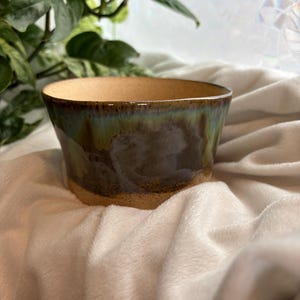 Maceta esmaltada verde y multicolor con orificio de drenaje y huella de mano esculpida.