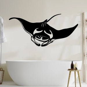 May include: Black and white silhouette of a manta ray, a type of fish, on a white wall above a white bathtub. The bathroom has a wooden side table with a bottle of lotion and a wooden shelf with various items.