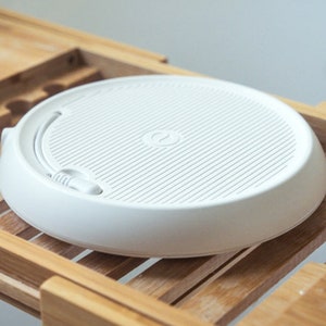 May include: White round charging base with a cord attached to the side. The base has a textured surface and a small logo in the center.