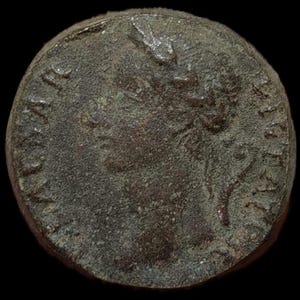 Puede incluir: Una moneda de color bronce desgastado con un perfil en relieve de una persona, posiblemente un gobernante, mirando hacia la derecha. La superficie de la moneda muestra signos de edad y desgaste, con texto visible en los bordes. Fondo negro.