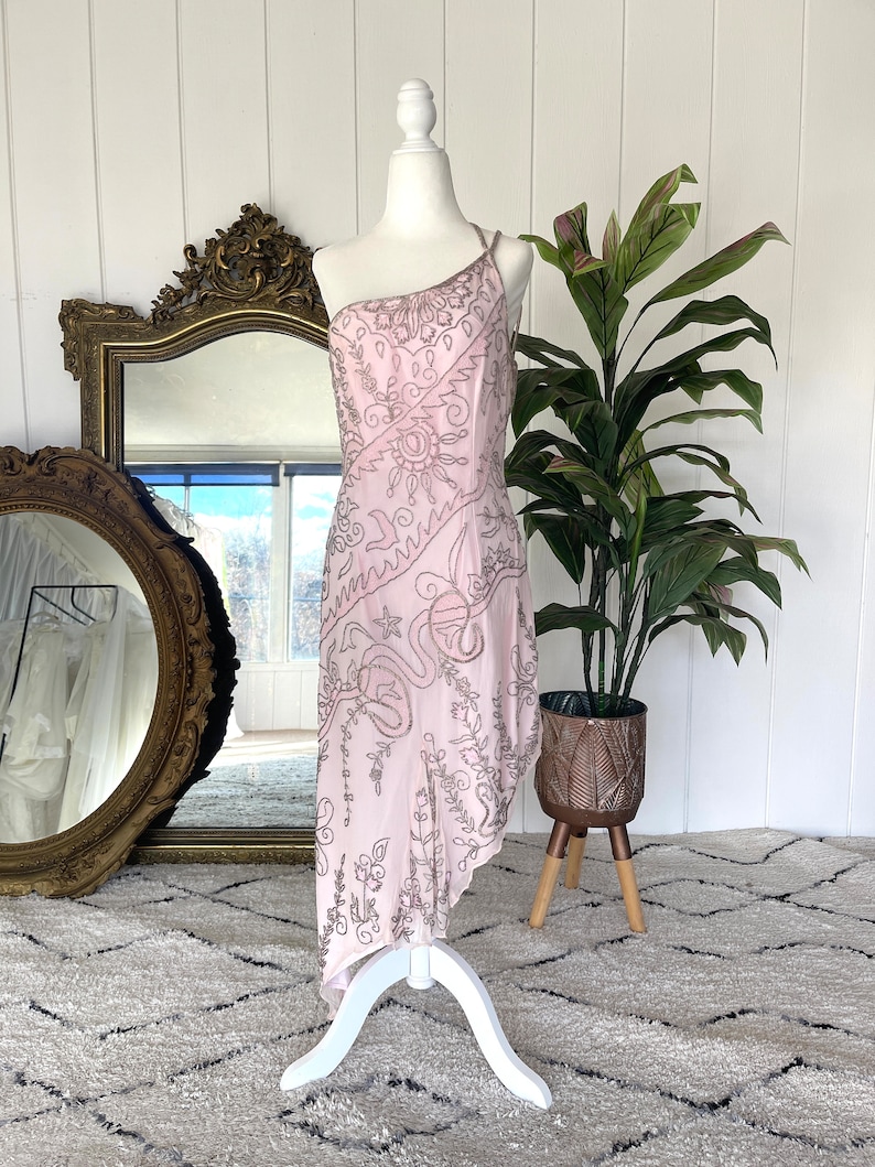 May include: A pink one-shoulder dress with a beaded design. The dress has a flowing, asymmetrical hemline.