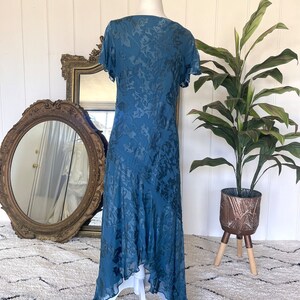 May include: A teal blue maxi dress with a floral pattern. The dress has a V-neckline, short sleeves, and a high-low hemline.