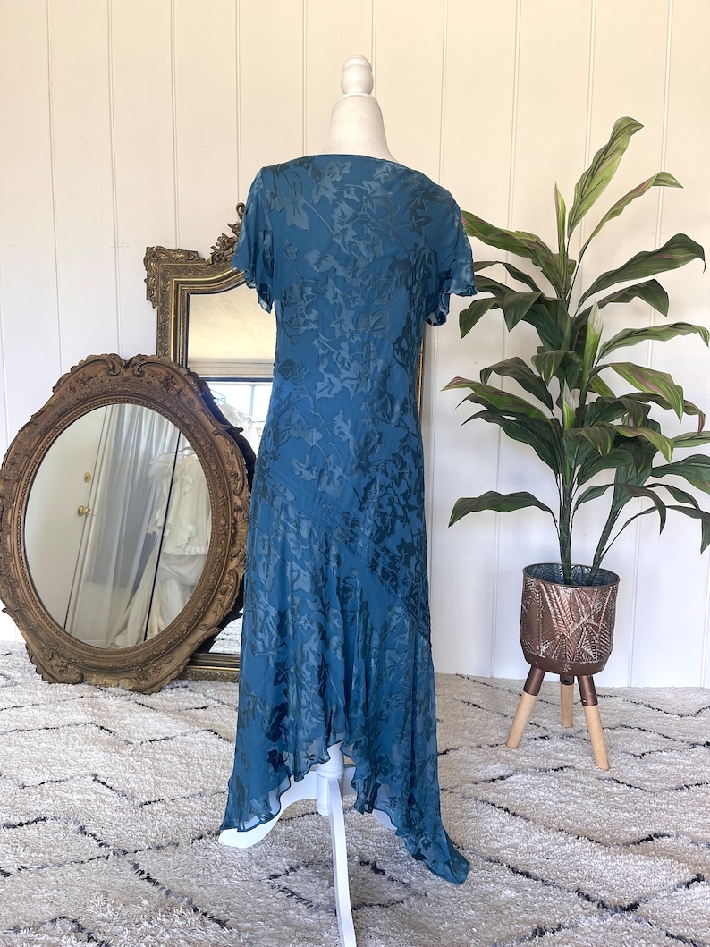 May include: A teal blue maxi dress with a floral pattern. The dress has a V-neckline, short sleeves, and a high-low hemline.