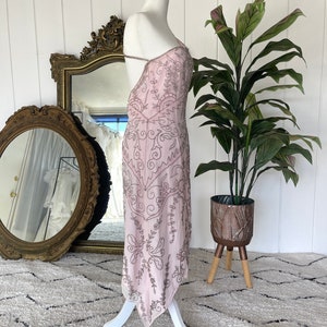 May include: A pink, beaded, sleeveless dress with a plunging neckline and a flowing skirt. The dress is on a white mannequin and has a delicate, intricate design.